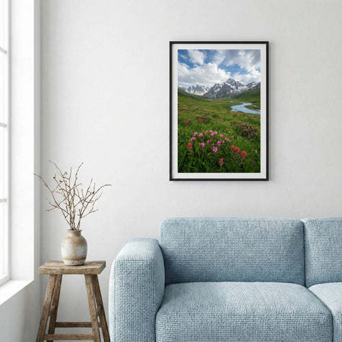 Pink wildflowers beside a mountain stream with snow-capped peaks beyond — framed canvas wall art in a wooden frame, 16×24 in