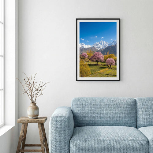 Pink blossom trees in a green meadow beneath snow-capped mountain peaks — framed canvas wall art in a wooden frame, 16×24 in