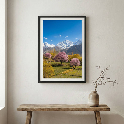 Pink blossom trees in a green meadow beneath snow-capped mountain peaks — wooden frame canvas wall art print, 12×18 in