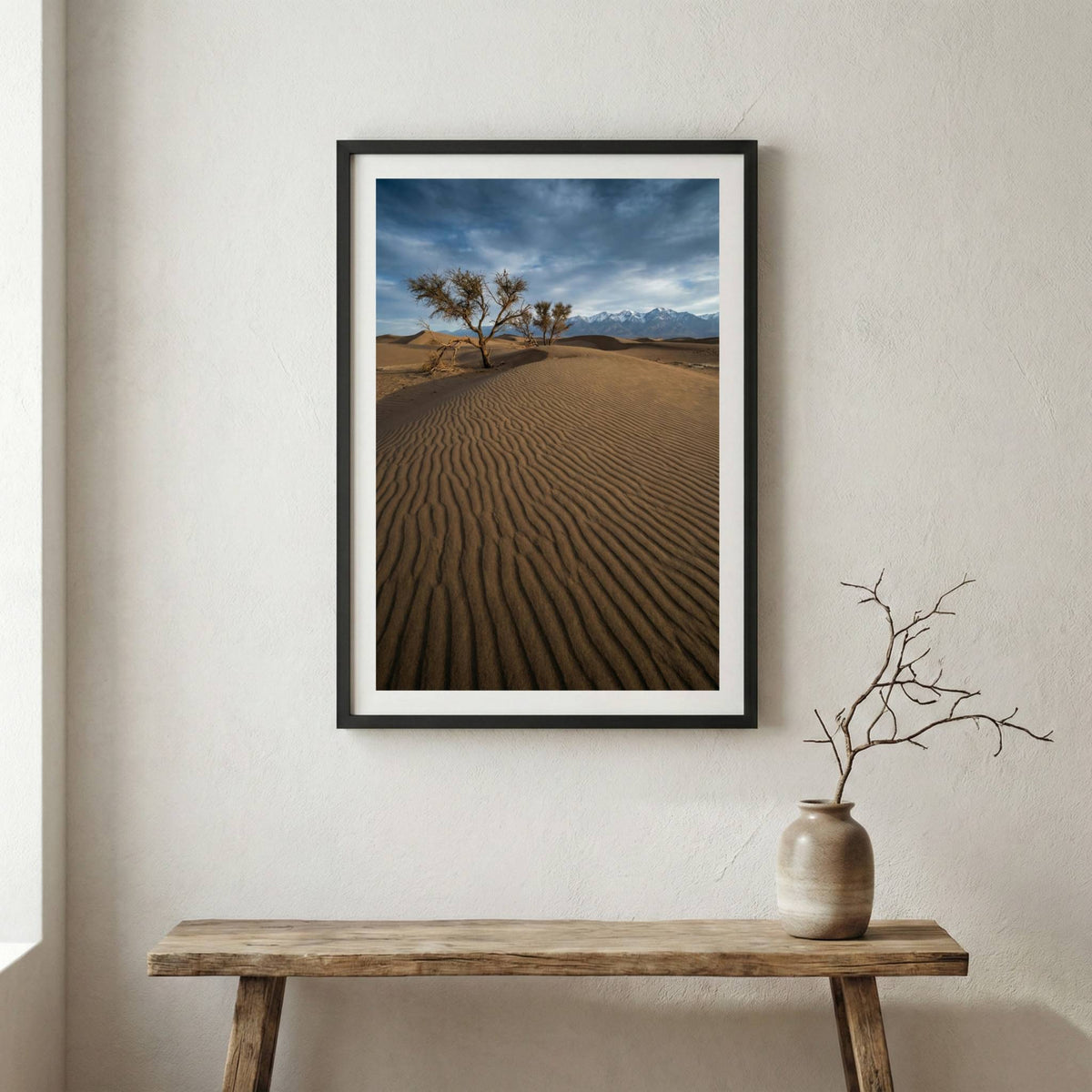 Lone bare tree on rippled desert dunes with distant snow-capped mountains — wooden frame canvas wall art print, 12×18 in