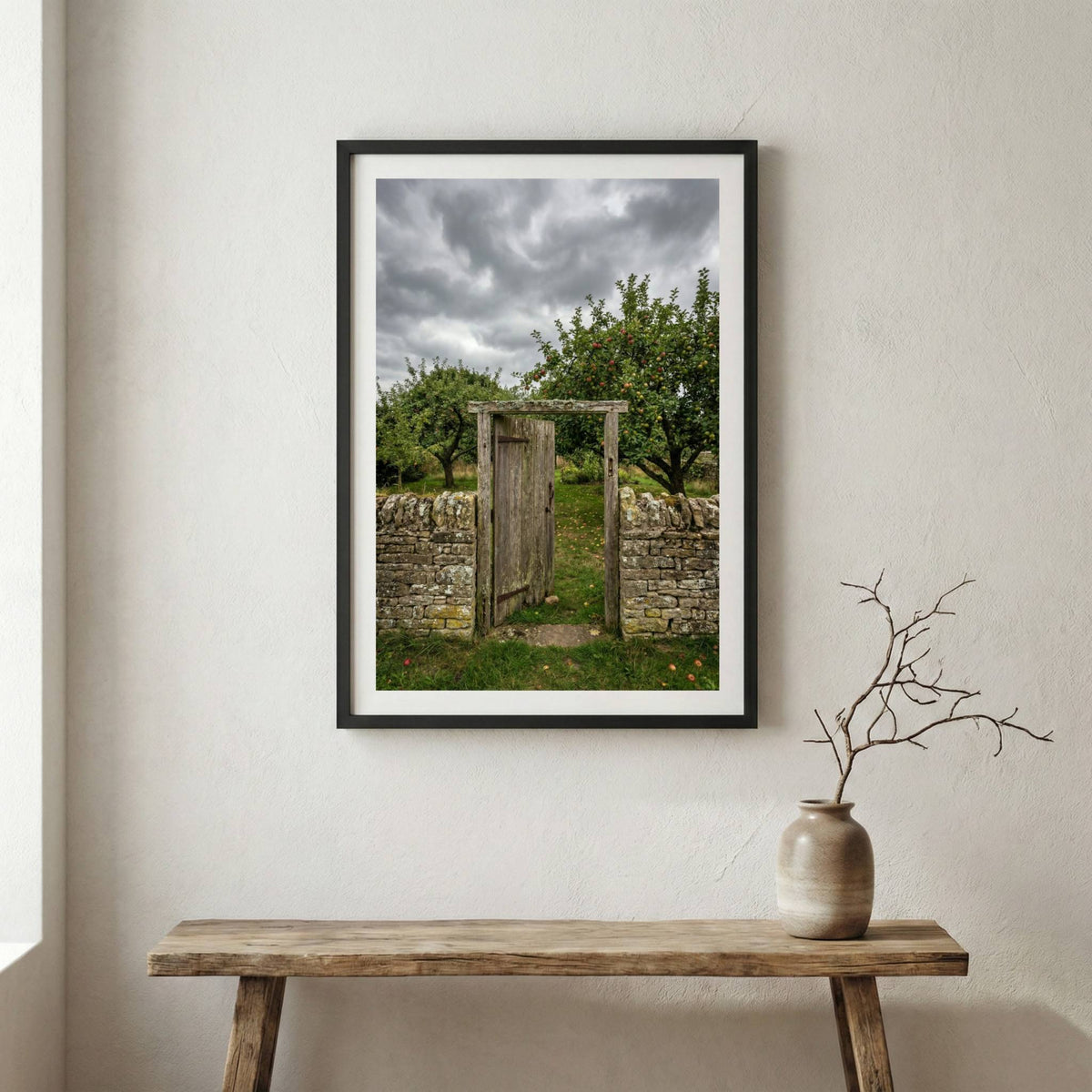 Weathered wooden gate in a stone wall opening onto a green orchard under a stormy sky — wooden frame canvas wall art print, 12×18 in