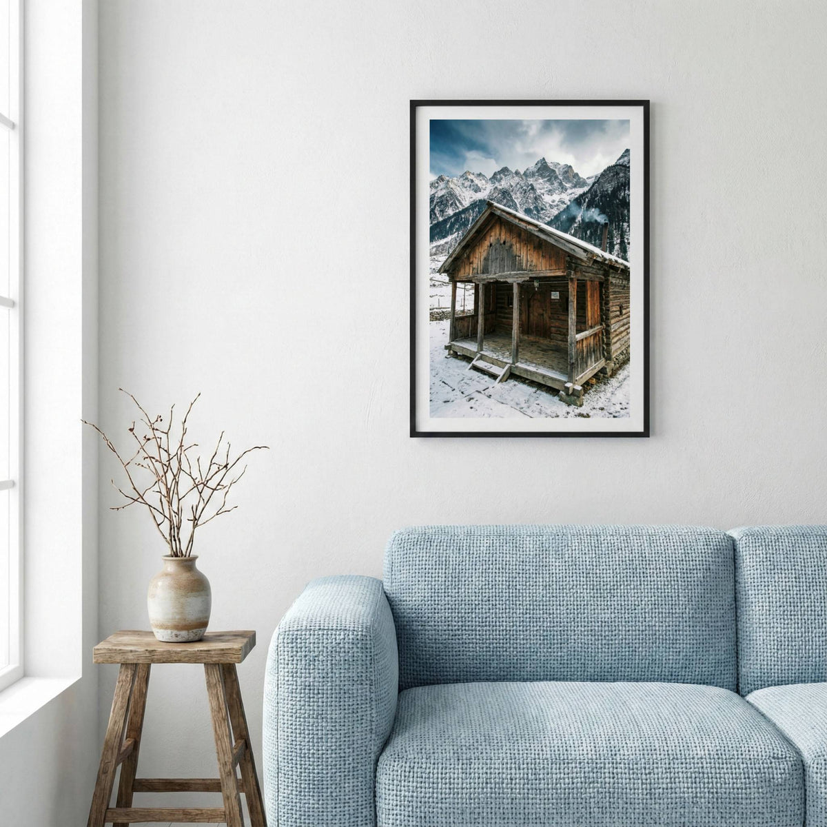 Snow-covered wooden cabin set against jagged, snow-capped mountains — framed canvas wall art in a wooden frame, 16×24 in